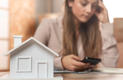Seorang wanita memegang kepala sambil melihat ponsel dengan miniatur rumah (www.freepik.com)