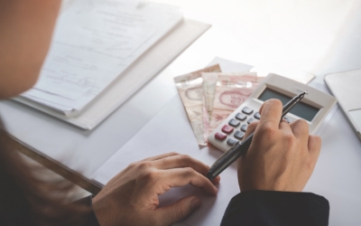 Seorang pria menghitung keuangan dengan pena, kalkulator, dan uang di mejanya (freepik.com)