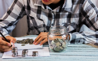 Seorang pria menghitung uang koin dengan stoples kaca diatas meja (freepik.com)